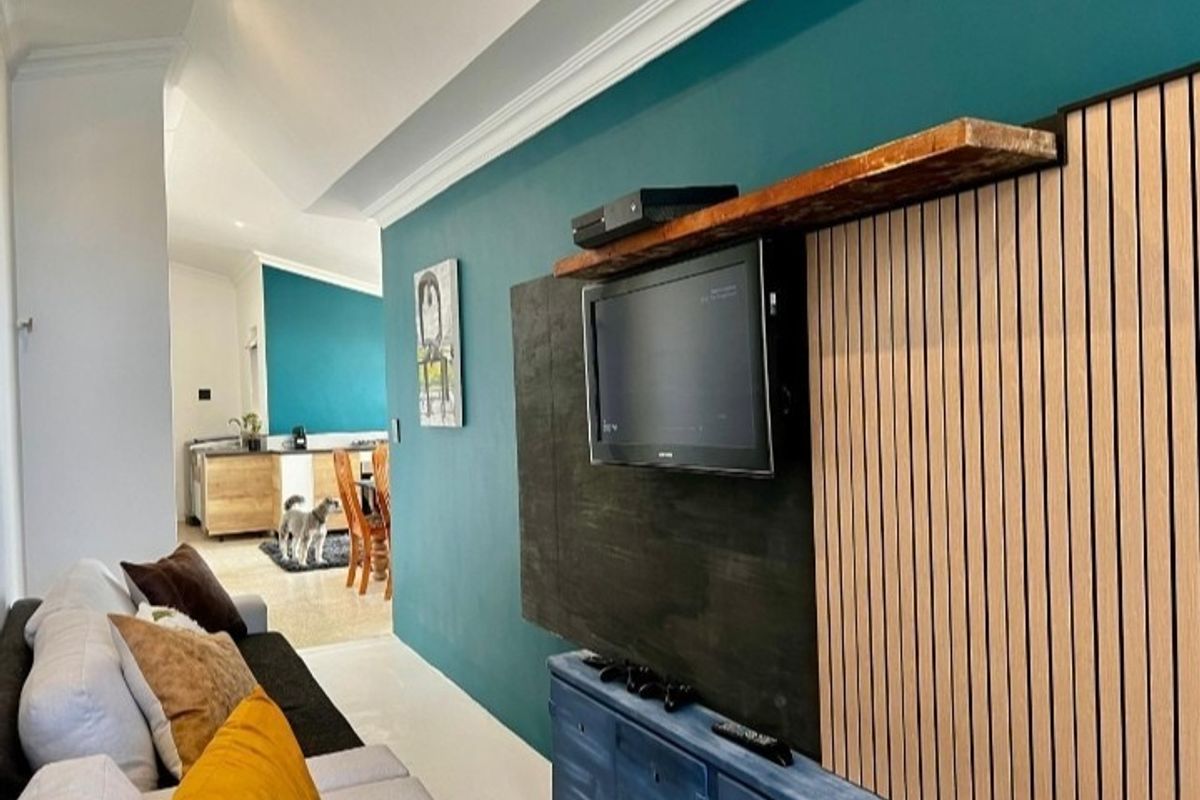 A modern living room featuring a decorative slatted timber feature wall with a floating shelf and recessed ceiling lighting.