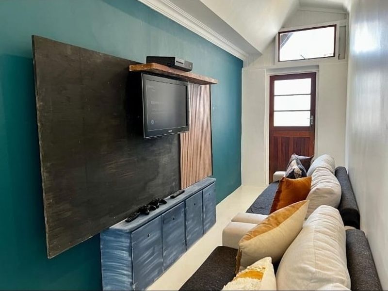 A narrow living room featuring a teal accent wall, built-in media cabinetry, a timber door, and a high-level clerestory window.