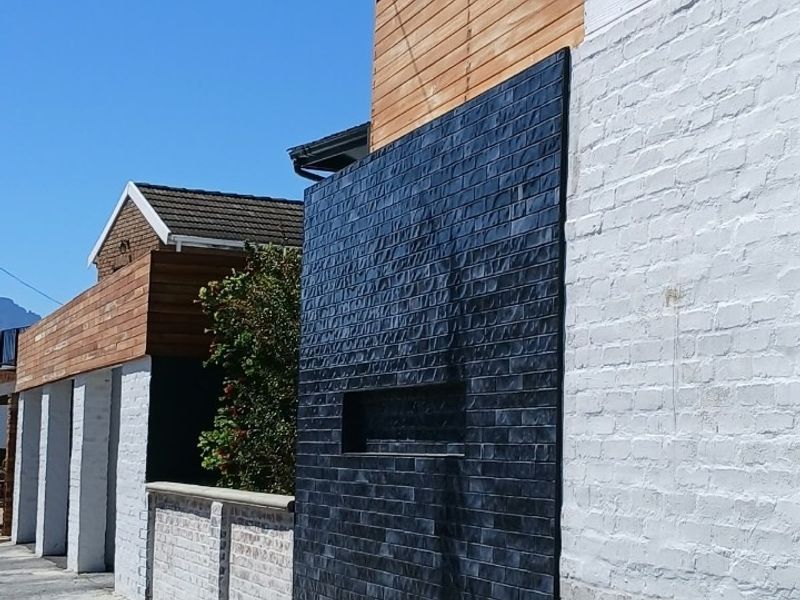Modern street-facing facade featuring a combination of painted brickwork, timber cladding, and a striking dark feature brick wall.
