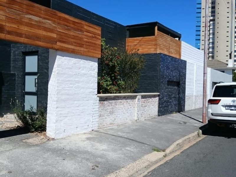 Street-level view of the property facade featuring a mix of painted brickwork and timber cladding with a boundary wall.