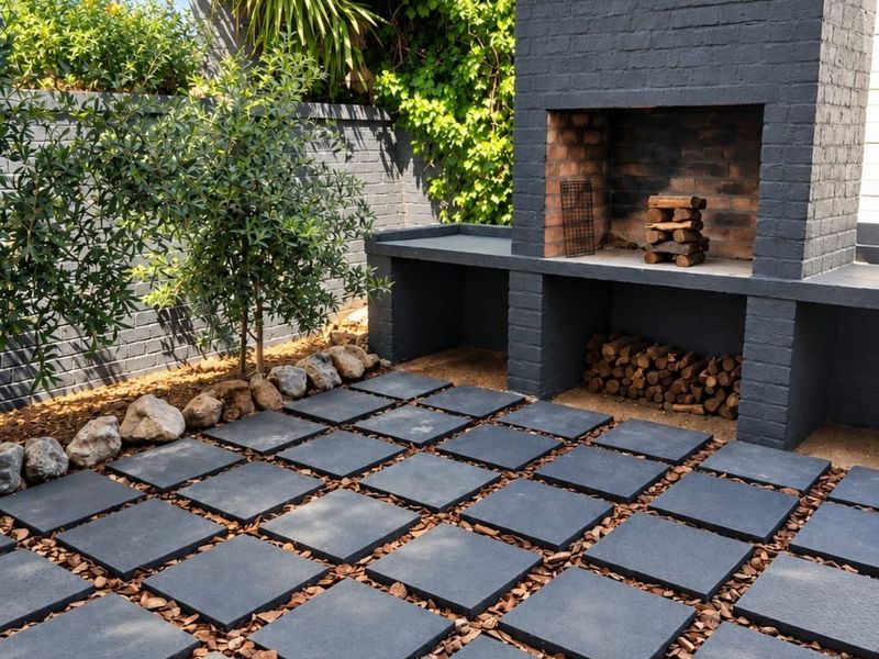 A well-maintained outdoor patio area featuring a modern built-in brick fireplace, concrete bench seating, and stylish square paver flooring.
