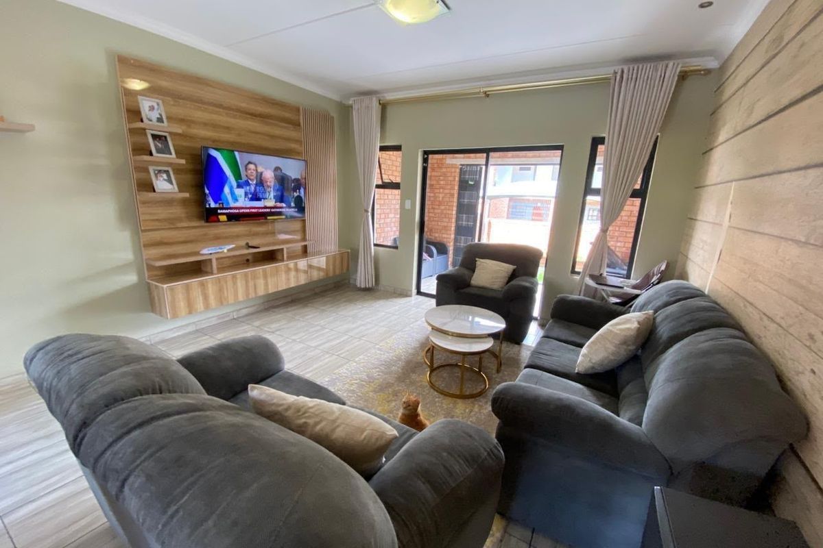 A comfortable living room featuring a built-in media unit, wood-look accent wall, tiled flooring, and sliding glass doors leading to an outdoor patio area.