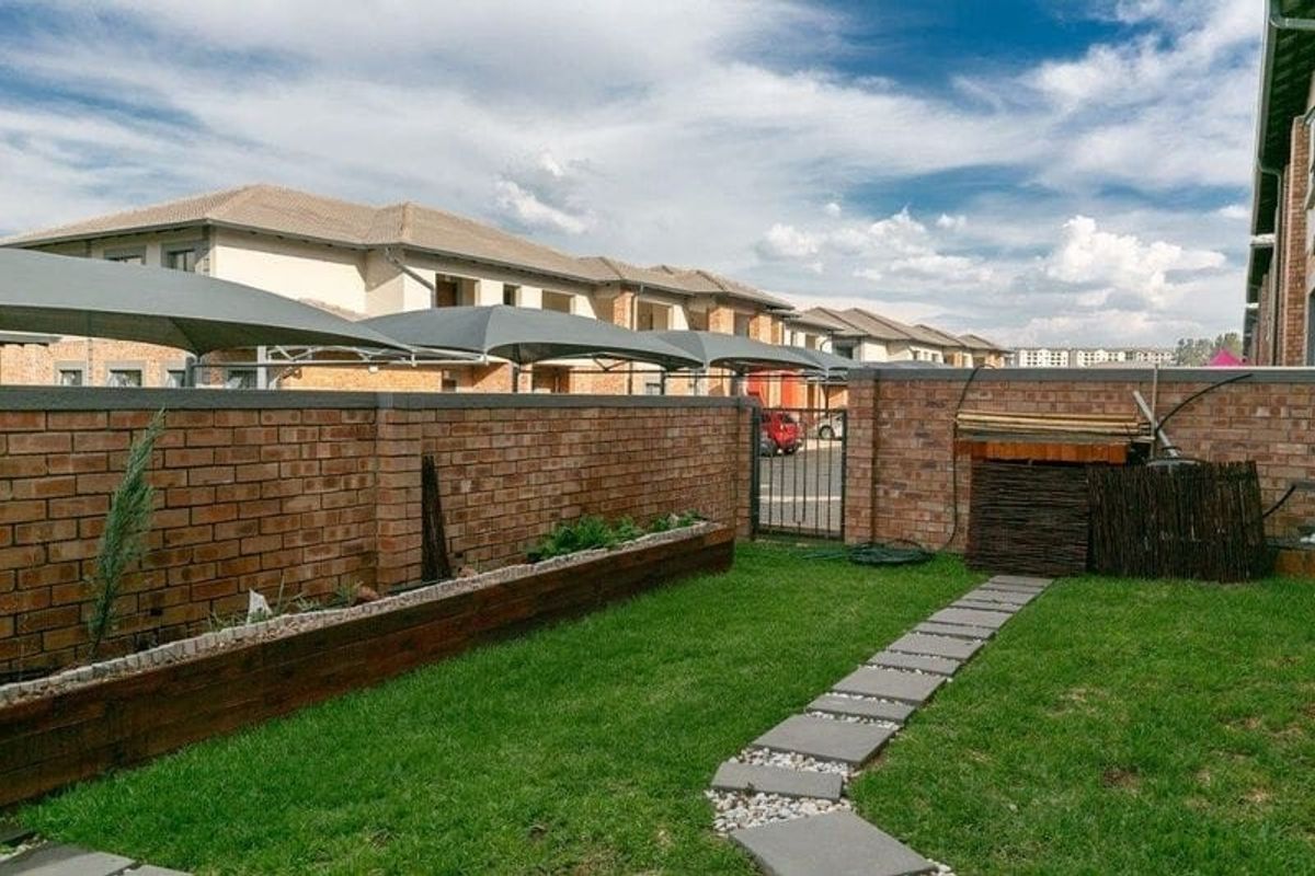 A private rear garden featuring a brick boundary wall, a stone paver pathway, and a raised timber garden bed.