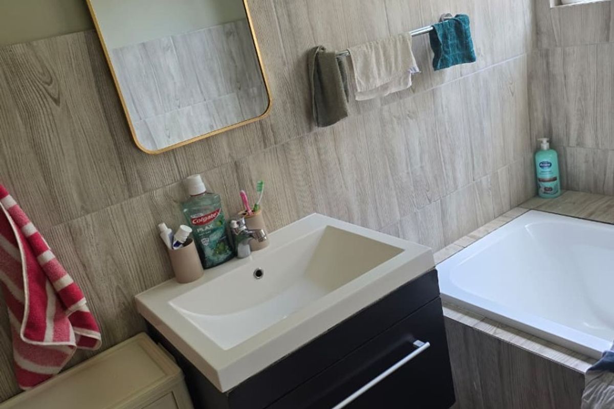 A modern bathroom featuring a floating vanity with basin, wood-look wall and floor tiling, and a built-in bathtub.