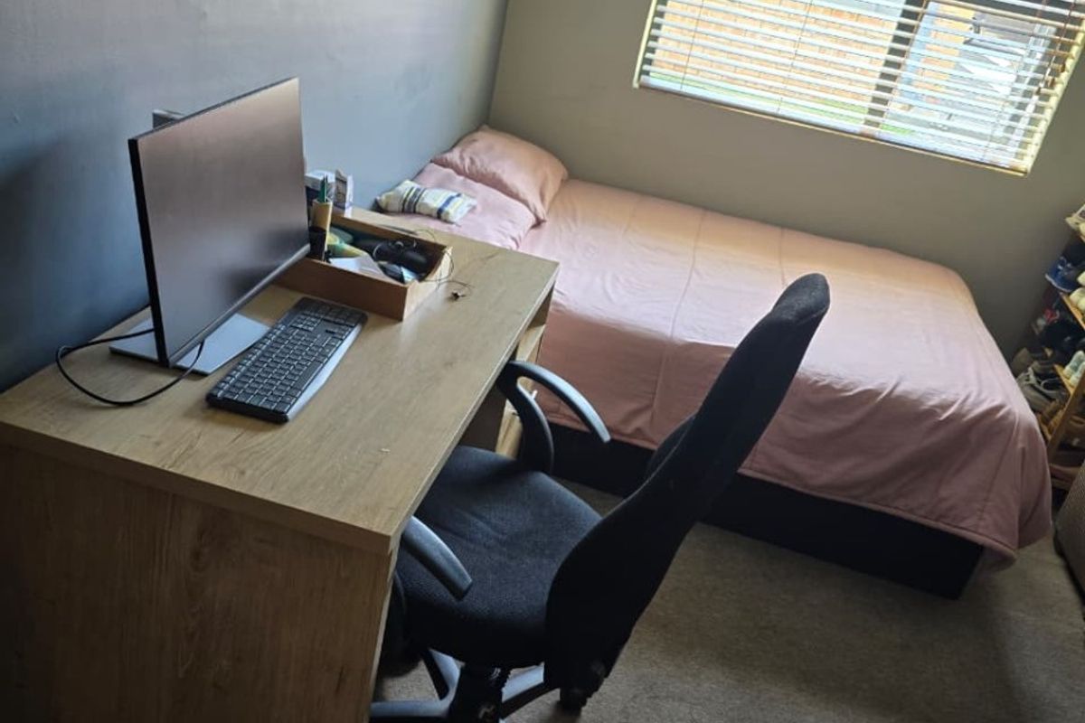 A functional bedroom featuring carpeted flooring and a window fitted with venetian blinds, providing natural light and a neutral backdrop.