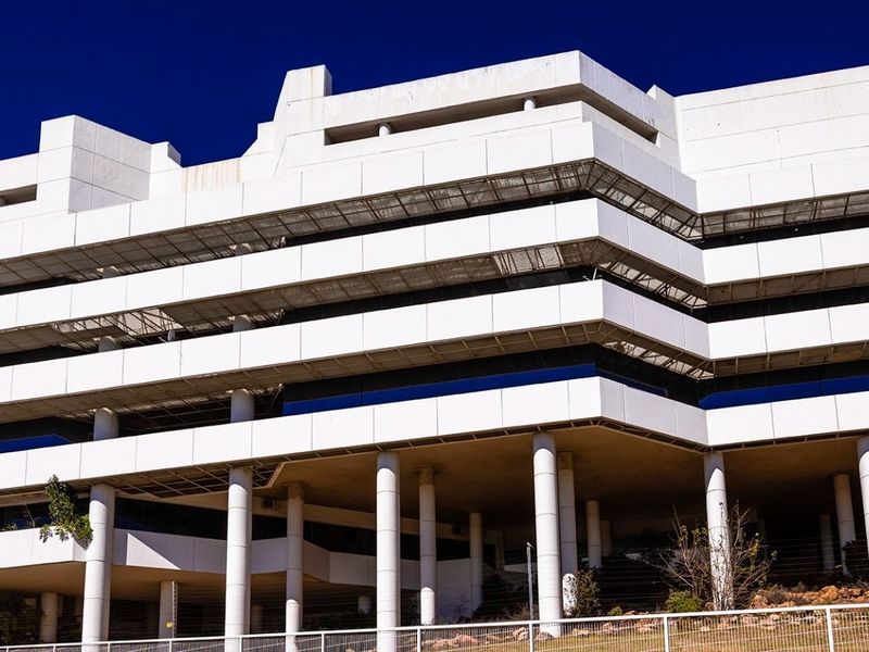 A modern multi-story commercial office building featuring a distinctive tiered white facade, ribbon windows, and an open-plan covered ground level.