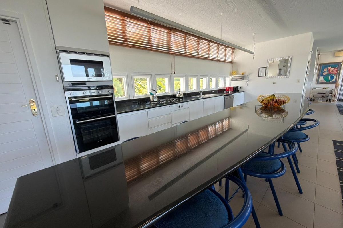 Modern kitchen featuring a long granite breakfast bar, built-in double oven, microwave, and a sleek row of windows providing natural light.
