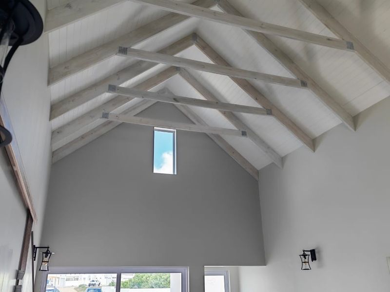 Spacious living area featuring a high vaulted ceiling with exposed timber trusses, tongue and groove paneling, and a modern clerestory window.