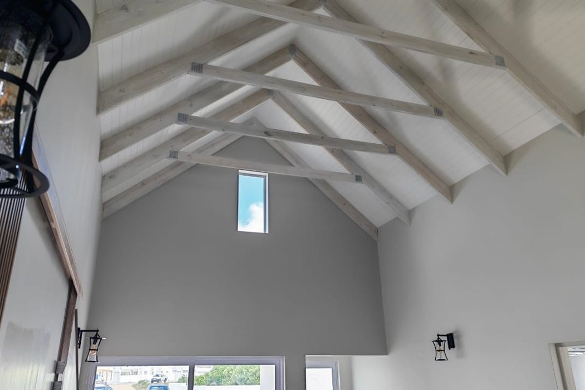 Spacious living area featuring a high vaulted ceiling with exposed timber trusses, tongue and groove paneling, and a modern clerestory window.