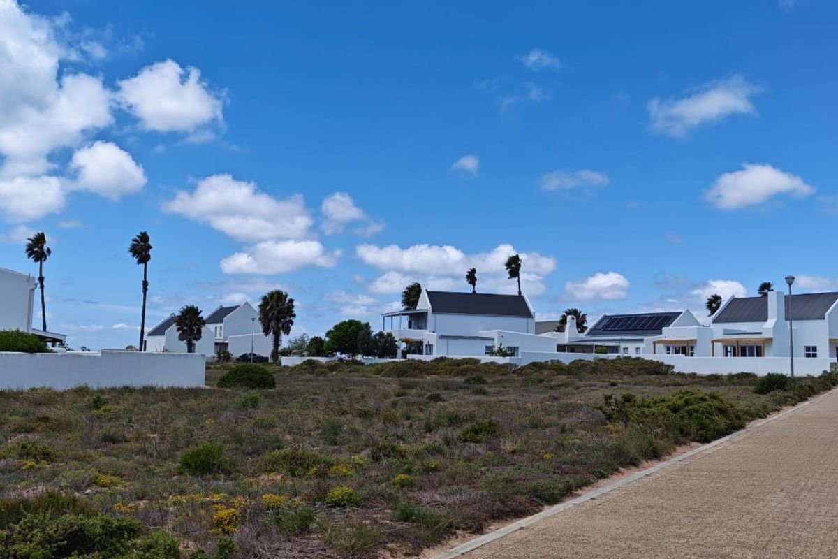 A view of the rear exterior of the property, showcasing white building facades, pitched roofs, solar panels, and a paved walkway.