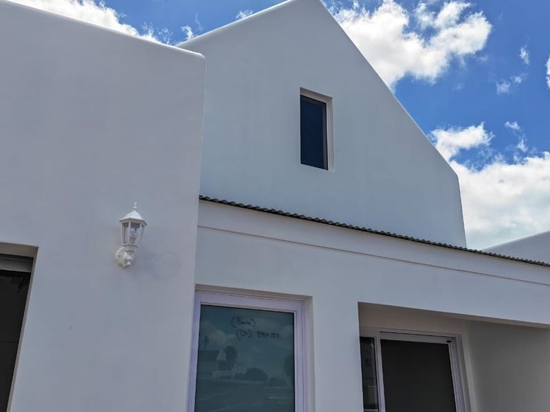 A modern, white-rendered exterior facade featuring a gabled roof design, clean lines, and contemporary sliding glass doors.
