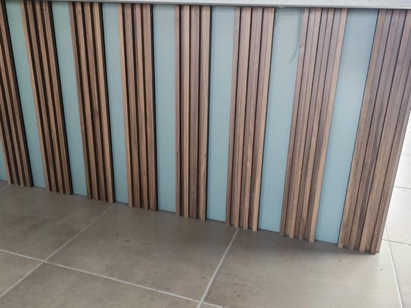 A close-up view of a modern kitchen island featuring contemporary vertical timber slat detailing and neutral porcelain floor tiles.