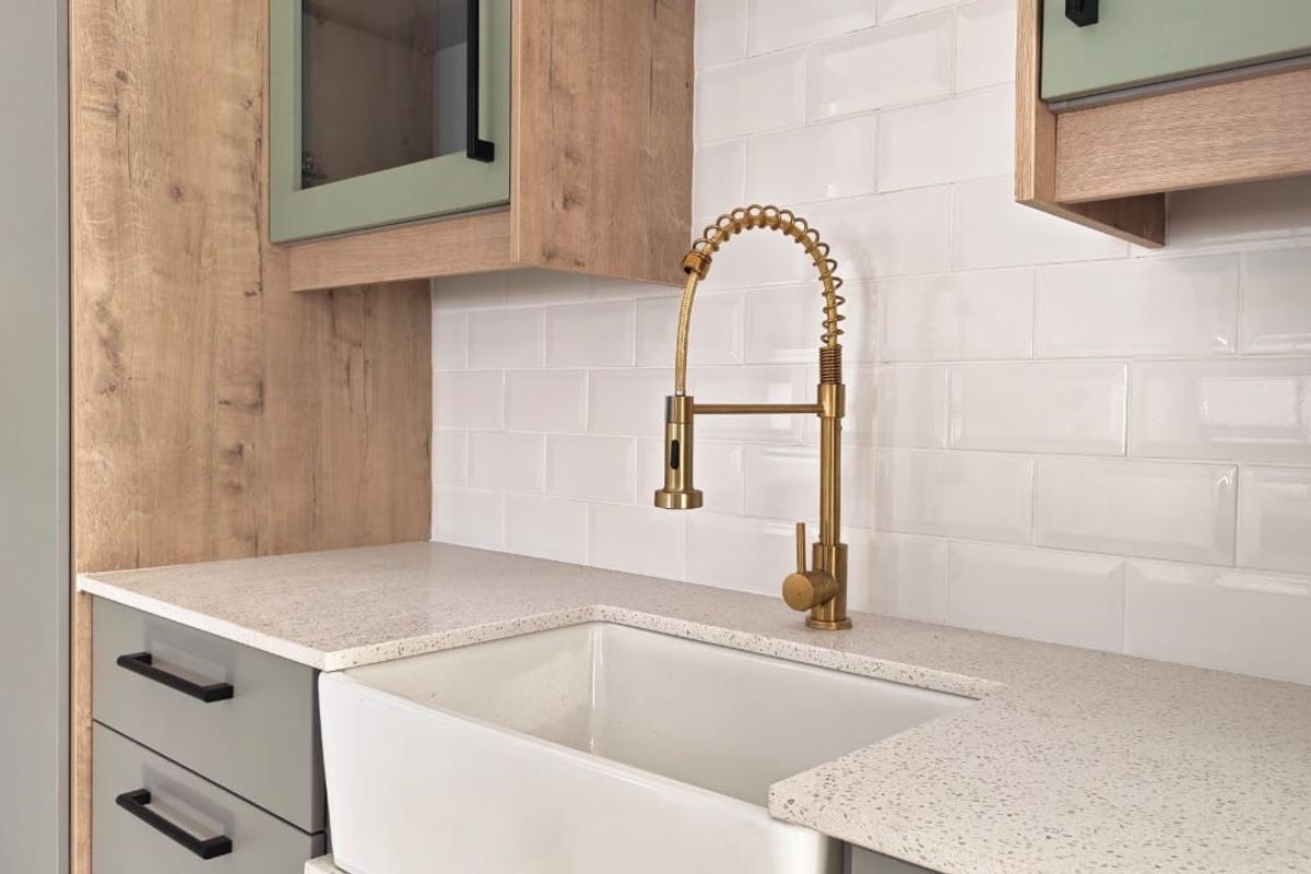 Modern kitchen featuring a farmhouse sink, brass gooseneck faucet, quartz countertops, and a classic white subway tile backsplash with custom cabinetry.