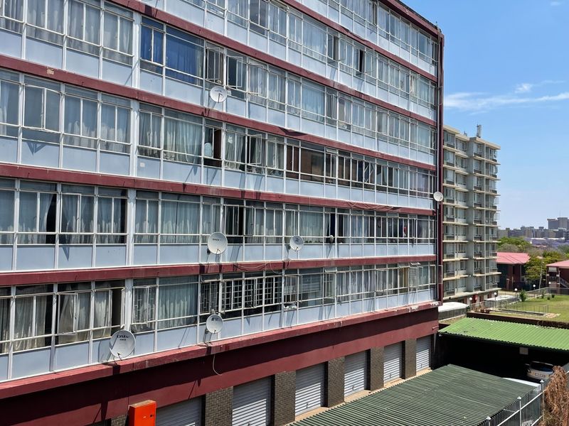 Exterior view of a multi-story apartment building featuring enclosed balconies, ground-level garages, and multiple satellite dish installations.