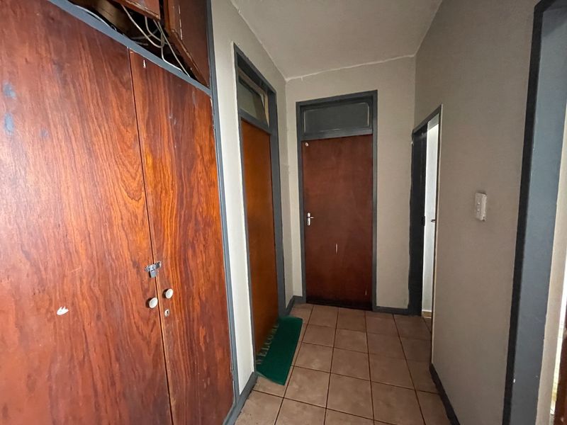 A functional hallway featuring tiled flooring, built-in wooden storage cupboards, and multiple internal access doors.