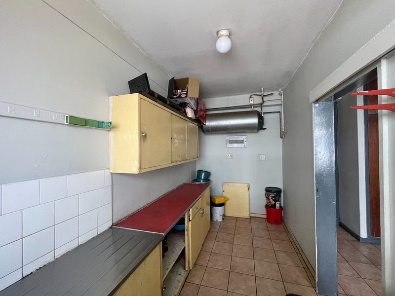 A functional scullery or utility area featuring built-in cabinetry, tiled splashbacks, and an exposed electric geyser, requiring cosmetic updates to improve its condition.