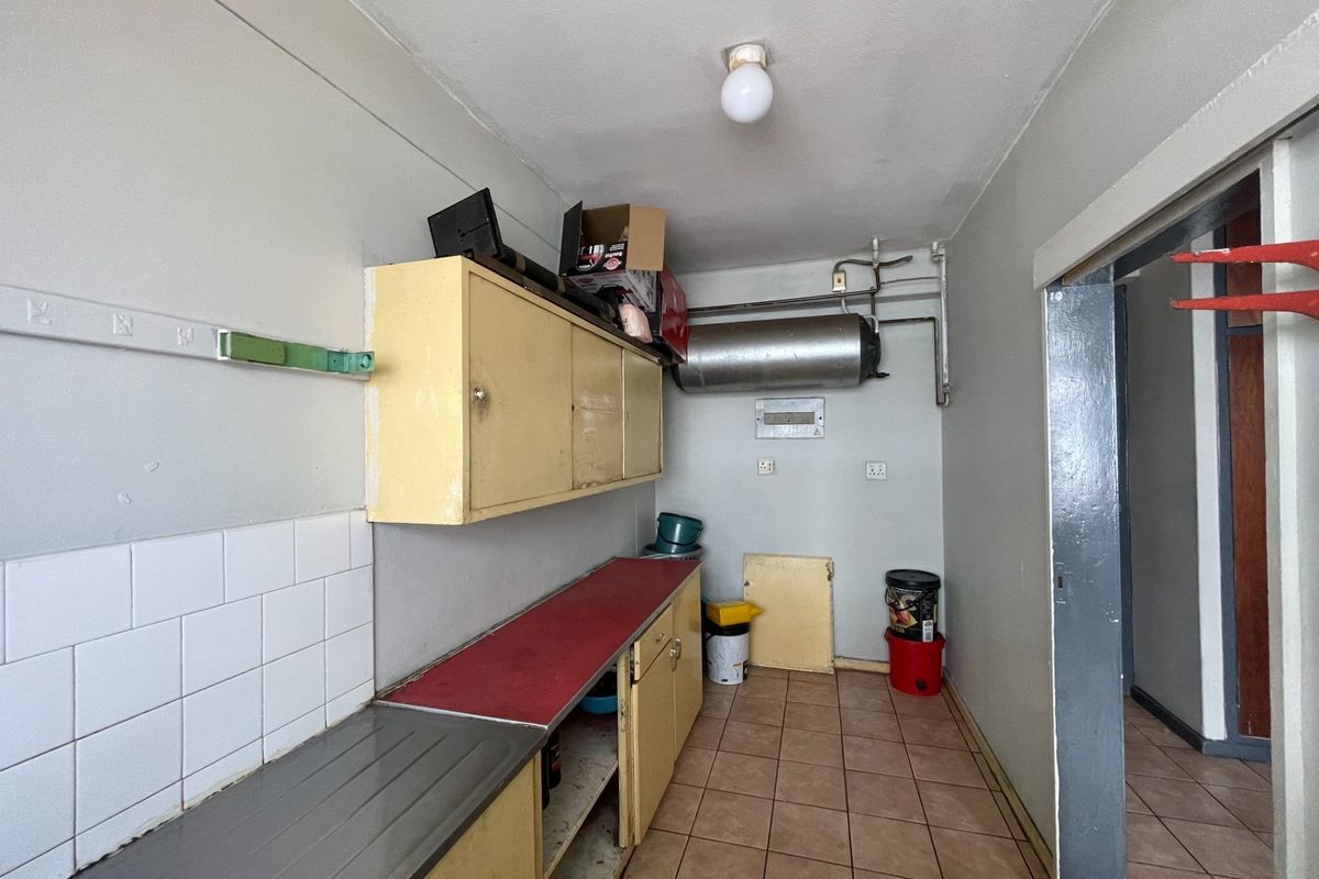 A functional scullery or utility area featuring built-in cabinetry, tiled splashbacks, and an exposed electric geyser, requiring cosmetic updates to improve its condition.