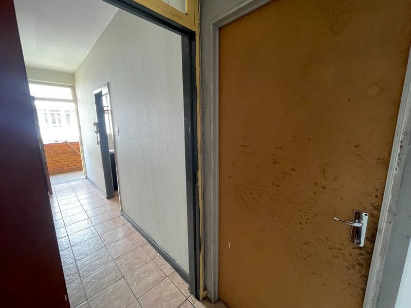 A functional hallway featuring tiled flooring and an internal door, showing signs of wear and requiring cosmetic updates.