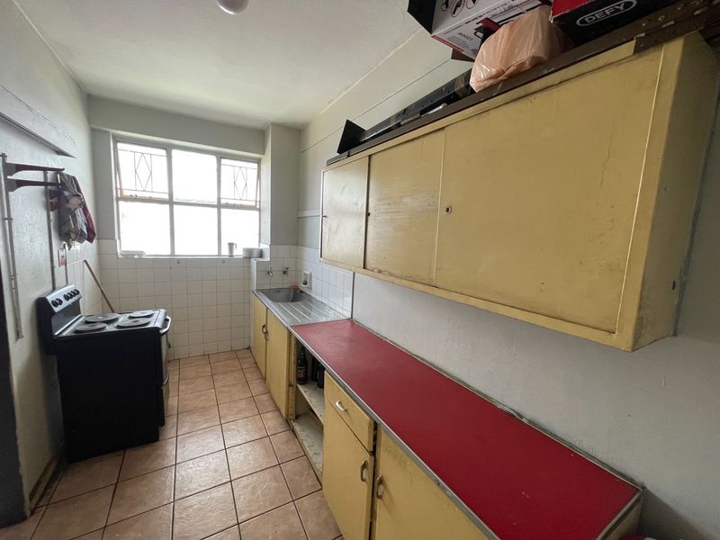 A dated kitchen featuring original cabinetry, a stainless steel sink, tiled splashbacks, and tiled flooring, offering significant potential for modernization and renovation.