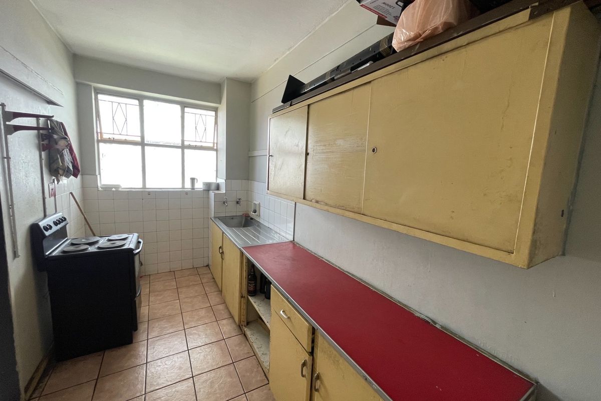 A dated kitchen featuring original cabinetry, a stainless steel sink, tiled splashbacks, and tiled flooring, offering significant potential for modernization and renovation.