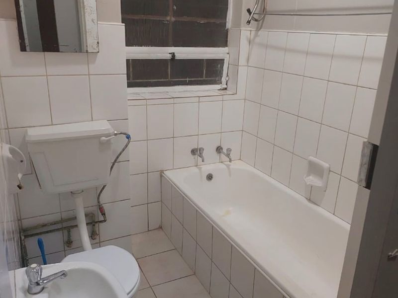 A compact, dated bathroom featuring a standard bathtub, pedestal basin, and toilet with white wall and floor tiling.