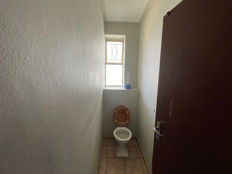 A compact, functional guest toilet featuring tiled flooring and a window with security bars, offering a blank canvas for potential cosmetic updates.