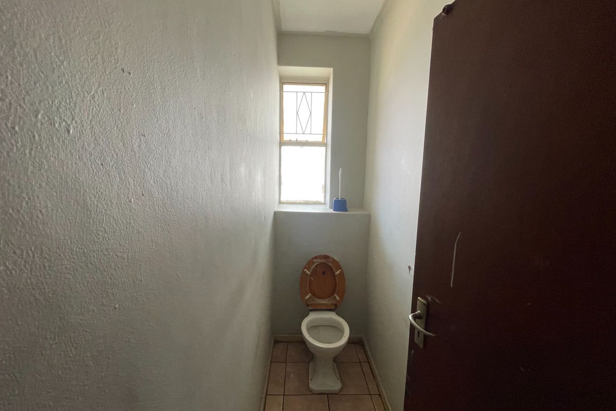 A compact, functional guest toilet featuring tiled flooring and a window with security bars, offering a blank canvas for potential cosmetic updates.