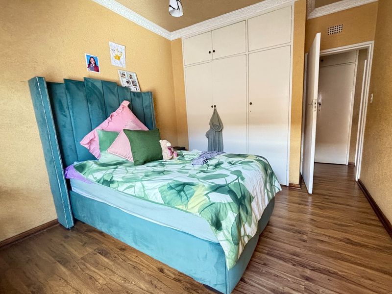 A bedroom featuring laminate flooring, built-in cupboards, and decorative ceiling cornicing, offering a functional space with potential for cosmetic updates.