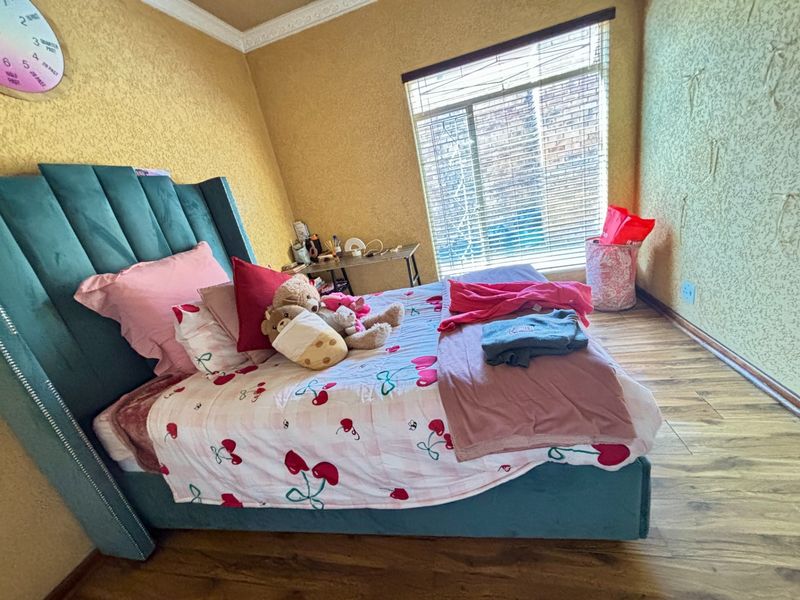 A bedroom featuring laminate flooring, crown molding, and a window with venetian blinds. The room has textured walls and standard electrical fixtures.
