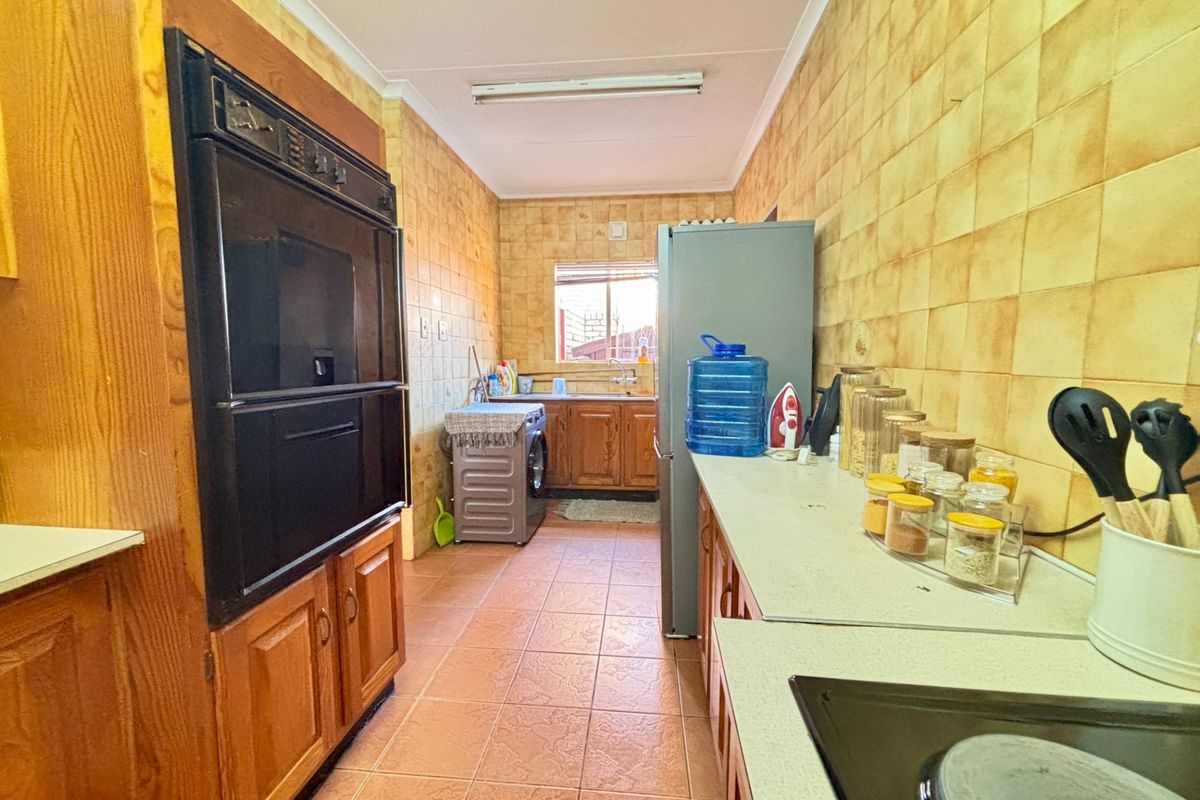 A functional galley-style kitchen featuring wooden cabinetry, built-in oven, ceramic hob, and tiled finishes throughout.