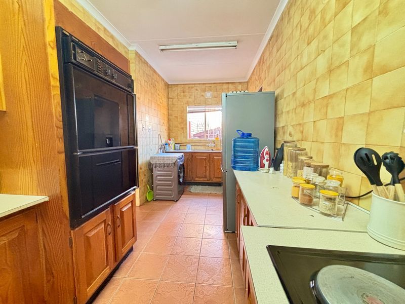 A functional galley-style kitchen featuring wooden cabinetry, built-in oven, ceramic hob, and tiled finishes throughout.