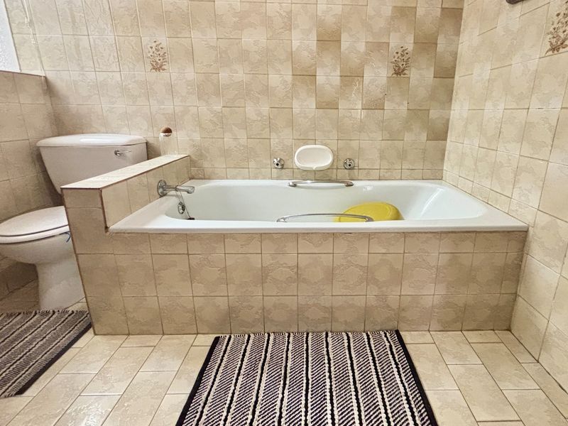 A functional bathroom featuring a built-in bathtub and toilet with neutral ceramic wall and floor tiling throughout.