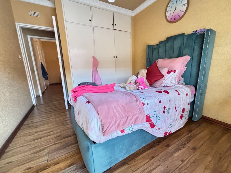 A bedroom featuring laminate flooring, built-in cupboards, and decorative ceiling cornicing, providing a functional and well-defined living space.