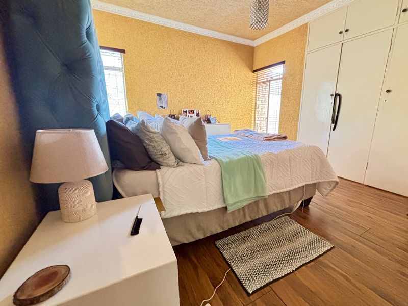 A bedroom featuring laminate flooring, built-in cupboards, and textured yellow walls with decorative ceiling cornicing.