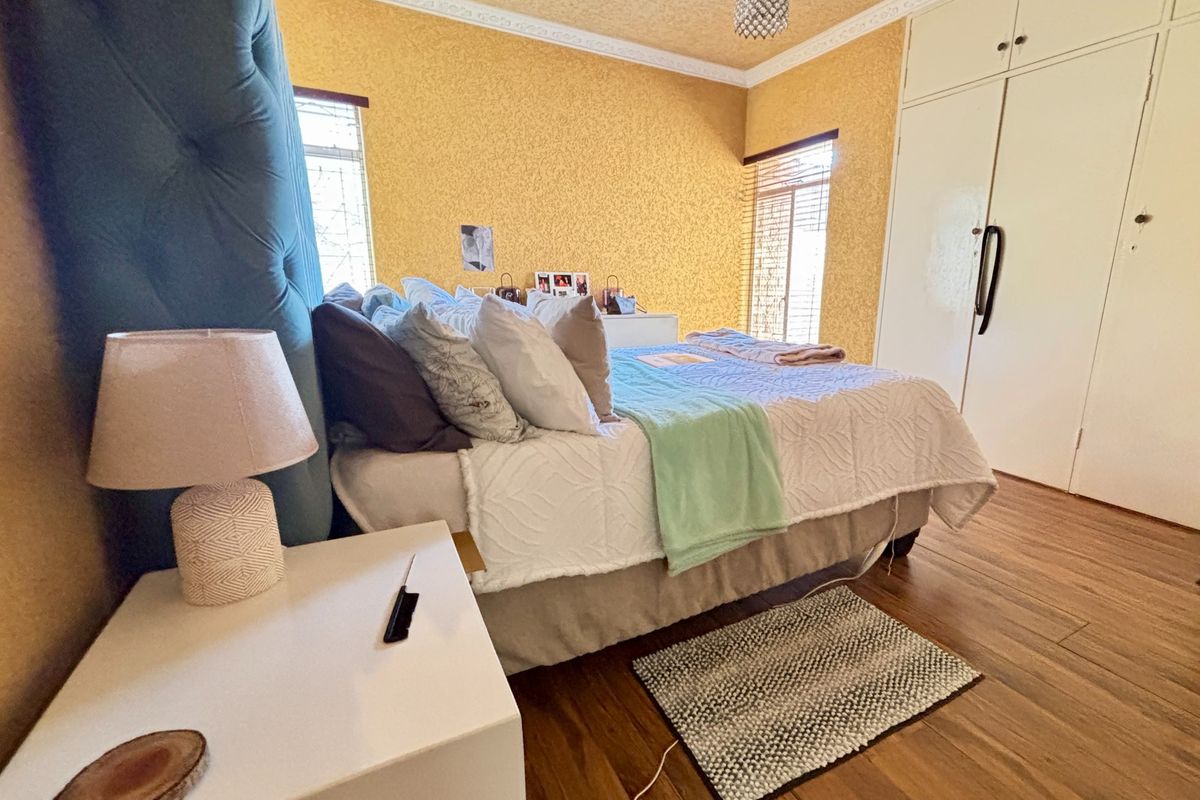 A bedroom featuring laminate flooring, built-in cupboards, and textured yellow walls with decorative ceiling cornicing.