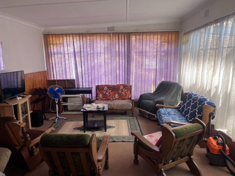 A living room featuring timber wall paneling and large windows with vertical blinds, offering a dated interior space ready for modernization.