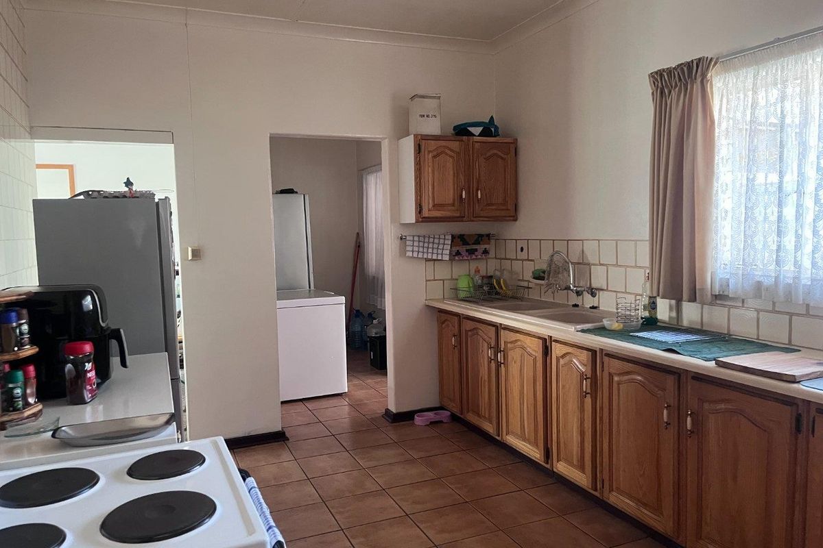 A functional kitchen featuring wooden cabinetry, tiled backsplash, and a double sink, with an adjacent utility area visible through the doorway.