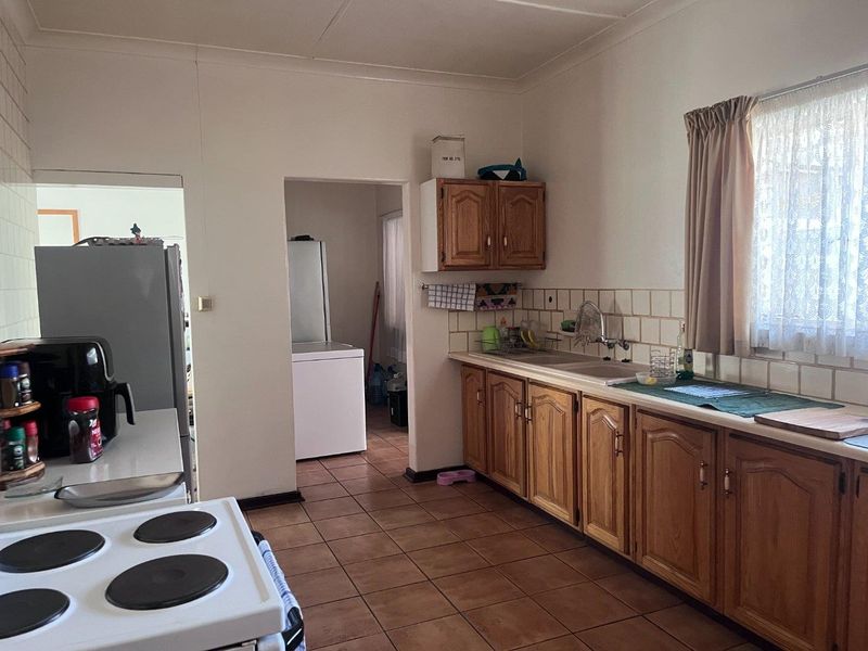 A functional kitchen featuring wooden cabinetry, tiled backsplash, and a double sink, with an adjacent utility area visible through the doorway.