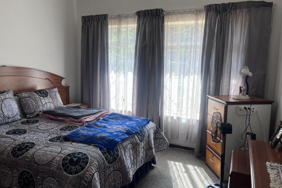 A functional bedroom featuring carpeted flooring and large windows fitted with security bars, providing natural light.