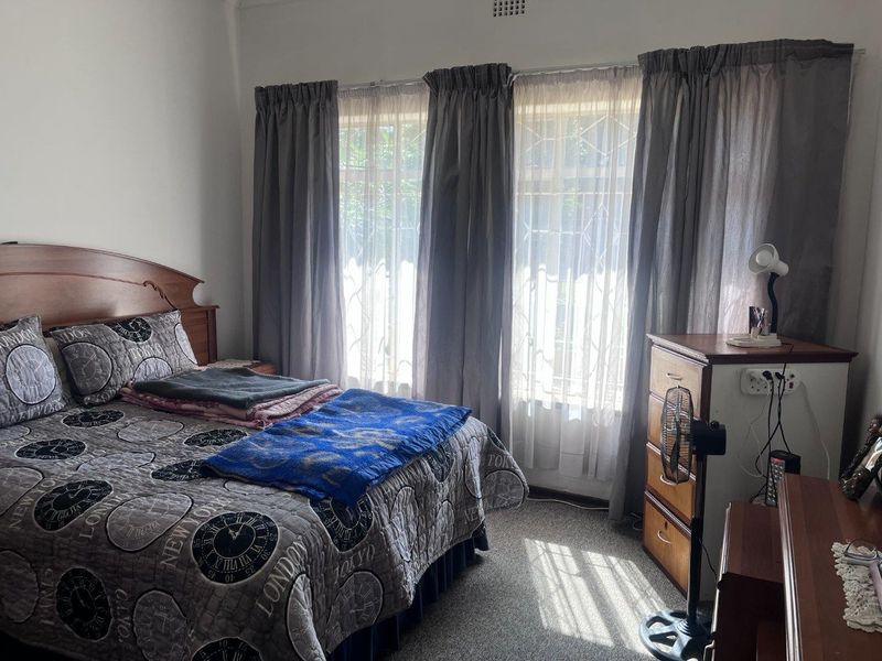 A functional bedroom featuring carpeted flooring and large windows fitted with security bars, providing natural light.