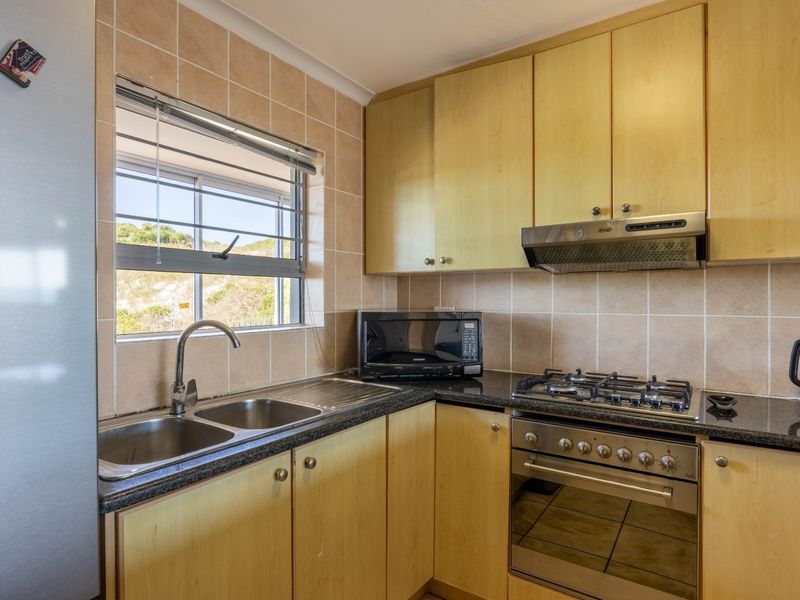 Functional kitchen featuring light wood cabinetry, granite countertops, a gas hob, built-in oven, and a double bowl stainless steel sink with tiled backsplash.