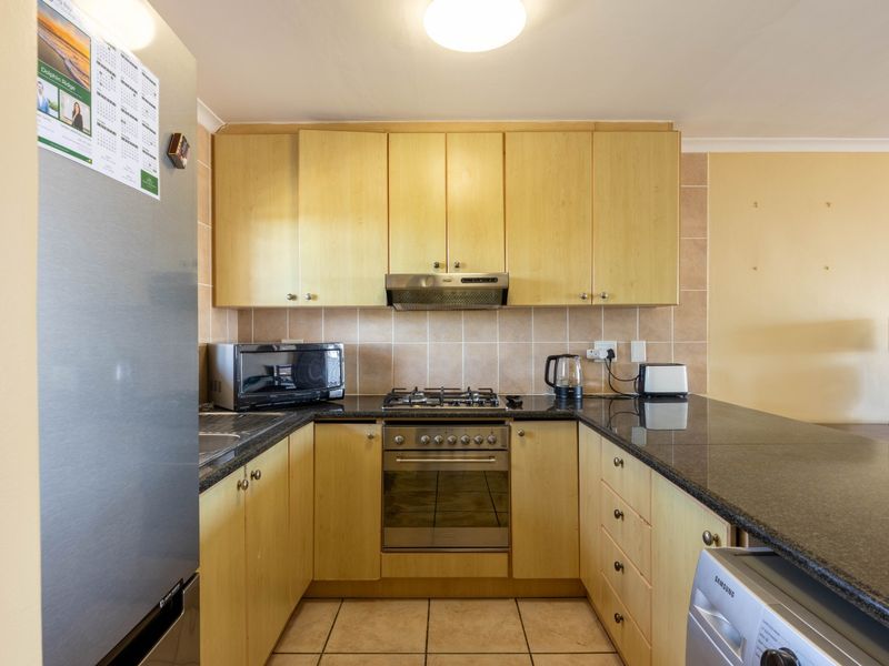 Functional kitchen featuring light wood cabinetry, granite countertops, a gas hob, built-in oven, and tiled backsplash with a breakfast bar extension.