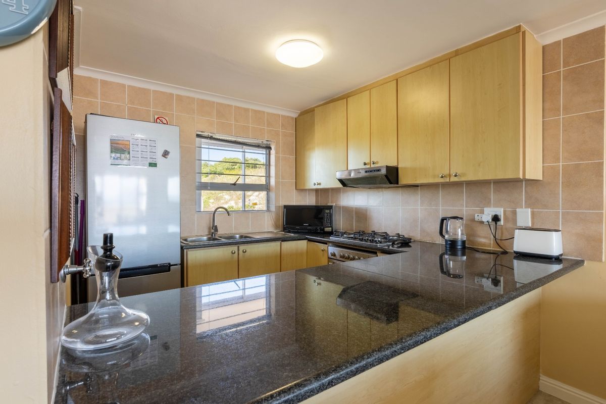 A functional kitchen featuring granite countertops, light wood-finish cabinetry, a gas hob with extractor fan, and a tiled backsplash.