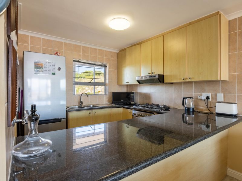 A functional kitchen featuring granite countertops, light wood-finish cabinetry, a gas hob with extractor fan, and a tiled backsplash.