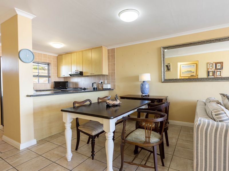 An open-plan living and dining area featuring tiled floors and a functional kitchen with built-in cabinetry and a tiled backsplash.