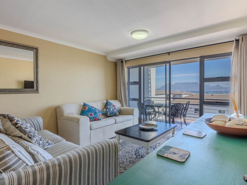 A comfortable living room featuring large sliding glass doors that provide access to a balcony and offer scenic mountain and sea views.