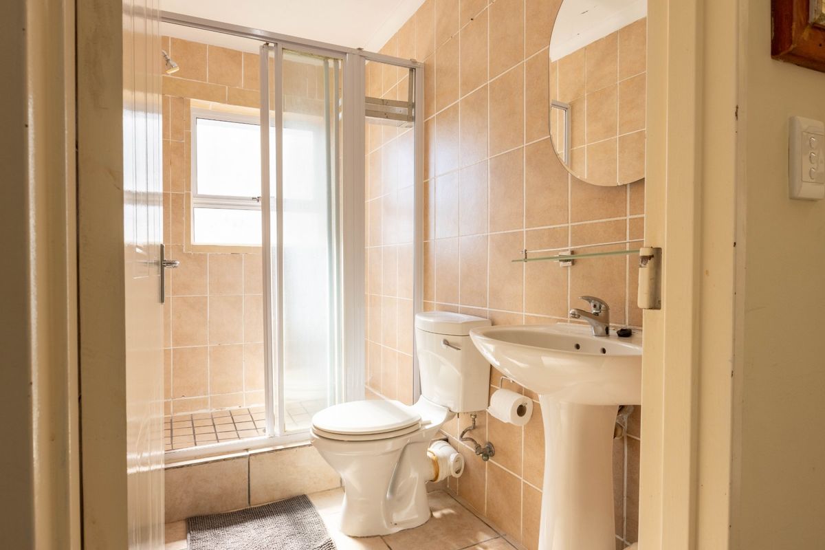 A functional bathroom featuring a pedestal basin, toilet, and a tiled shower enclosure with neutral wall tiling.
