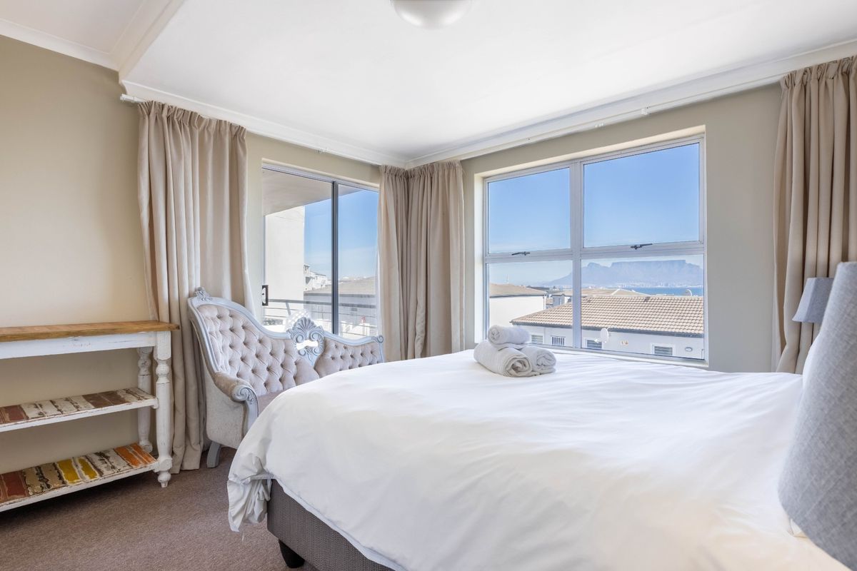 A bright and airy bedroom featuring large windows with scenic views, neutral wall tones, and carpeted flooring, offering a comfortable and well-lit living space.