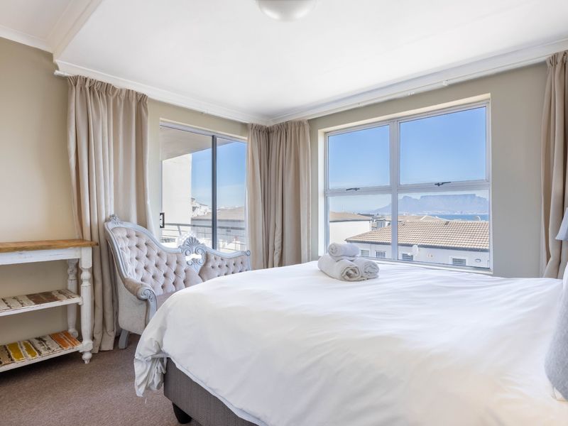 A bright and airy bedroom featuring large windows with scenic views, neutral wall tones, and carpeted flooring, offering a comfortable and well-lit living space.