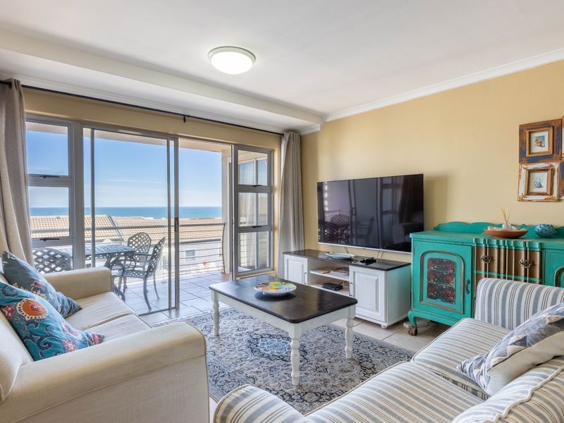 A bright living room featuring large sliding glass doors that open onto a balcony with ocean views and tiled flooring throughout.